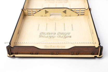 Minimalist wooden Slingshot game with bold Enchantoys branding, black and white striker pieces, and a spring-powered sling mechanism on both ends.