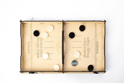 Wooden Slingshot Board Game by Enchantoys with black and white pucks placed across two playing fields. The board features a central slot and elastic bands for flick-based gameplay.